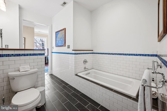 bathroom with visible vents, toilet, a bath, a wainscoted wall, and tile walls