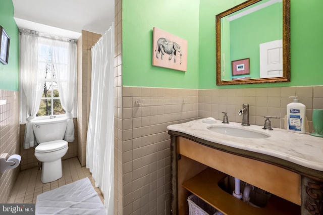 full bathroom featuring tile patterned flooring, toilet, vanity, tile walls, and wainscoting