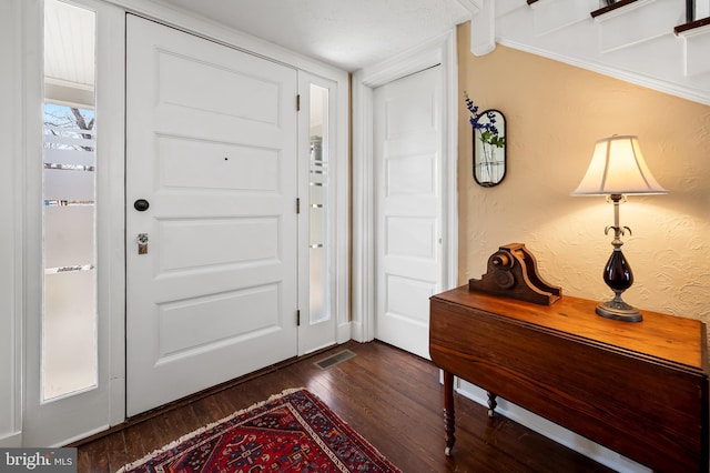 foyer entrance featuring dark wood-type flooring, visible vents, and a textured wall