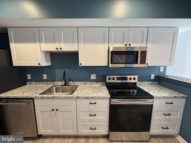 kitchen featuring appliances with stainless steel finishes, light wood-style flooring, a sink, and white cabinetry