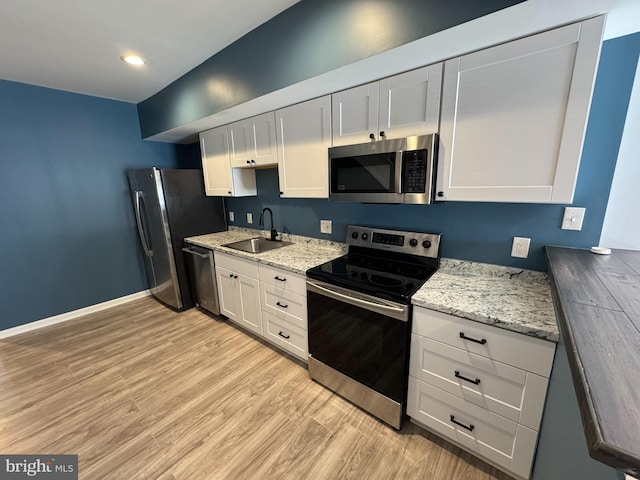 kitchen with light wood finished floors, baseboards, white cabinets, appliances with stainless steel finishes, and a sink