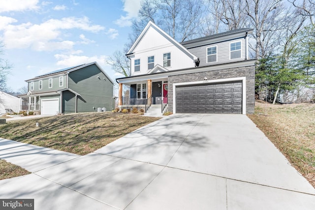 traditional home with driveway, stone siding, an attached garage, covered porch, and a front yard