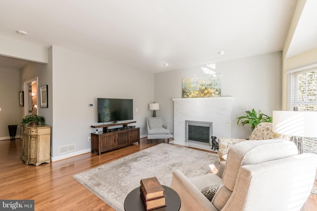 living room featuring light wood-type flooring, visible vents, baseboards, and a premium fireplace