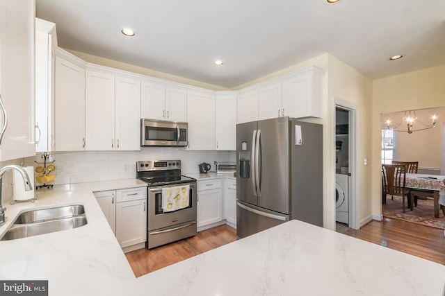 kitchen with washer / clothes dryer, appliances with stainless steel finishes, light wood-style floors, white cabinetry, and a sink