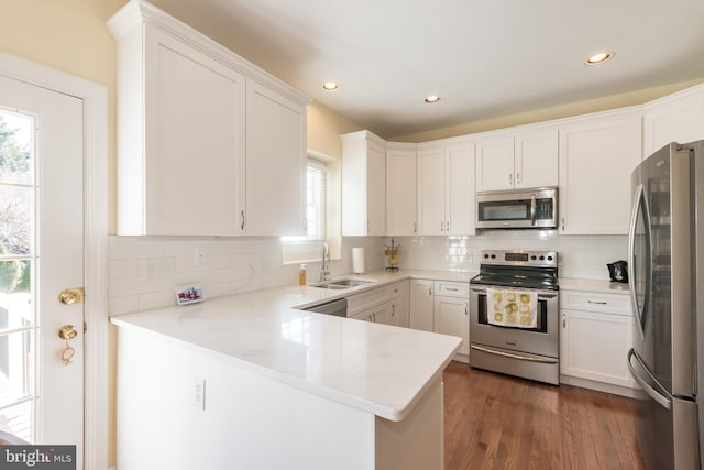 kitchen featuring a peninsula, appliances with stainless steel finishes, decorative backsplash, and a sink