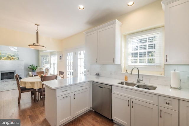 kitchen featuring stainless steel dishwasher, a sink, a glass covered fireplace, and tasteful backsplash