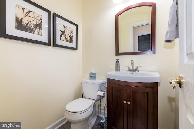 half bath with toilet, baseboards, and vanity