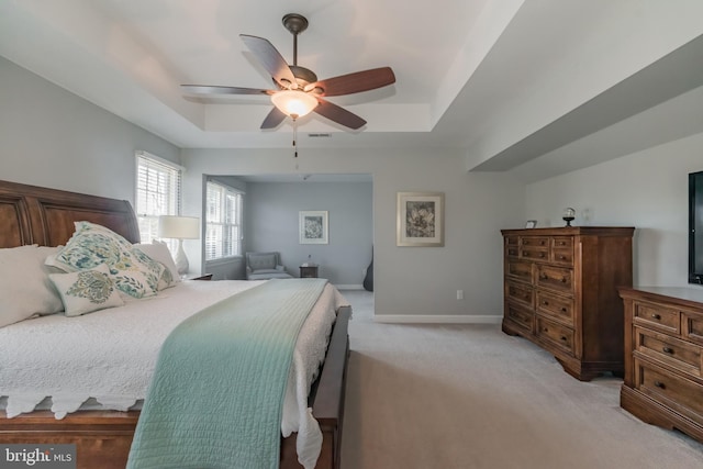 bedroom featuring a tray ceiling, light carpet, ceiling fan, and baseboards