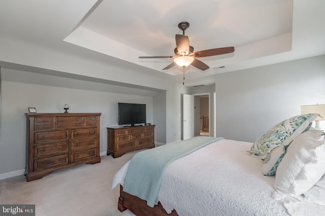 bedroom with light carpet, a tray ceiling, and baseboards