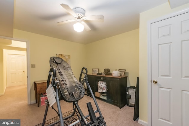 exercise room featuring light carpet, baseboards, and a ceiling fan