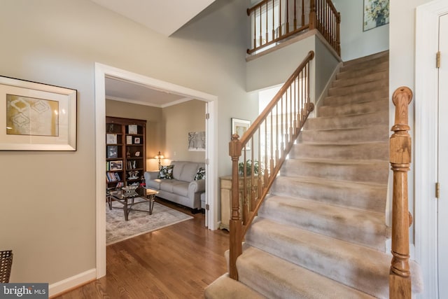 stairway with a towering ceiling, crown molding, baseboards, and wood finished floors