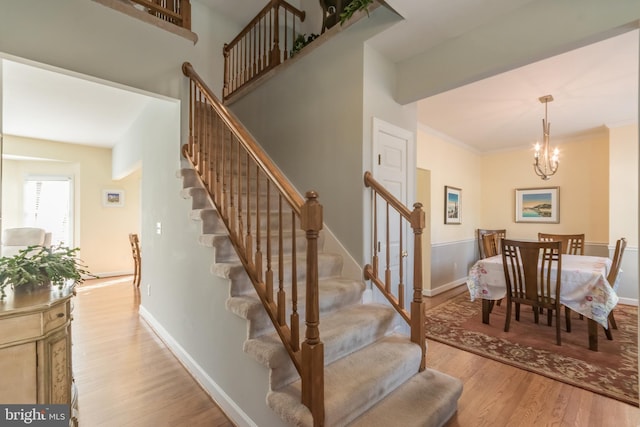 staircase featuring crown molding, a notable chandelier, wood finished floors, and baseboards