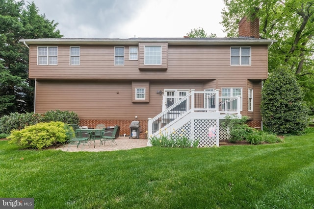rear view of property with a chimney, a patio area, stairs, and a lawn