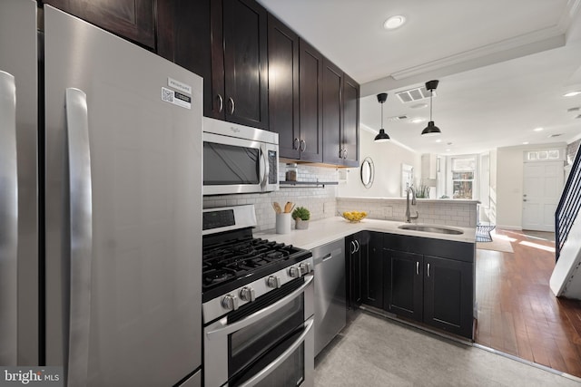 kitchen with appliances with stainless steel finishes, a sink, light countertops, pendant lighting, and backsplash