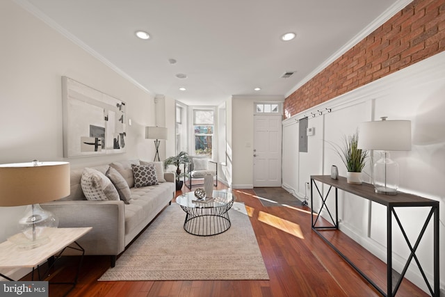 living area with brick wall, ornamental molding, dark wood-style flooring, and visible vents