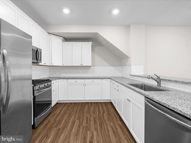 kitchen with dark wood finished floors, appliances with stainless steel finishes, white cabinetry, a sink, and light stone countertops