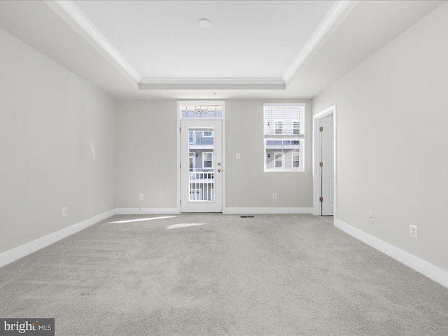 empty room with light carpet, baseboards, a raised ceiling, and crown molding