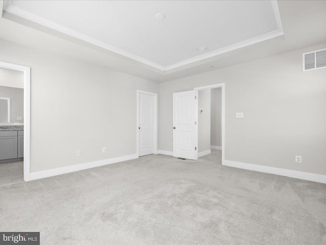 unfurnished bedroom with visible vents, a tray ceiling, baseboards, and light colored carpet