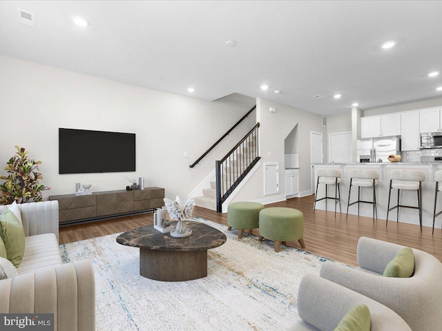 living area with stairs, wood finished floors, visible vents, and recessed lighting