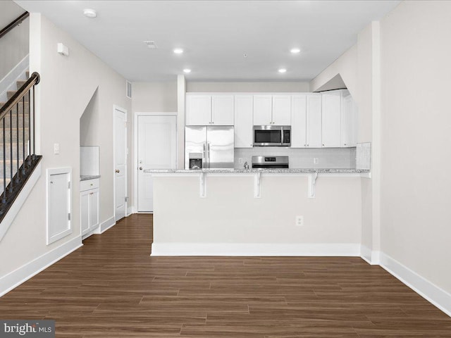 kitchen with light stone counters, a breakfast bar, stainless steel appliances, white cabinetry, and a peninsula