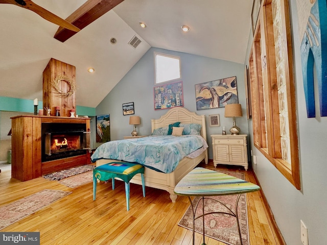 bedroom featuring a warm lit fireplace, visible vents, vaulted ceiling, and wood finished floors