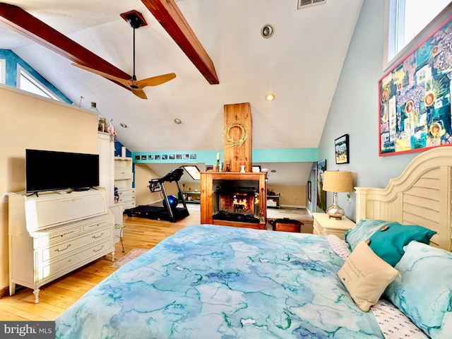 bedroom featuring vaulted ceiling with beams, a warm lit fireplace, light wood-style flooring, and visible vents