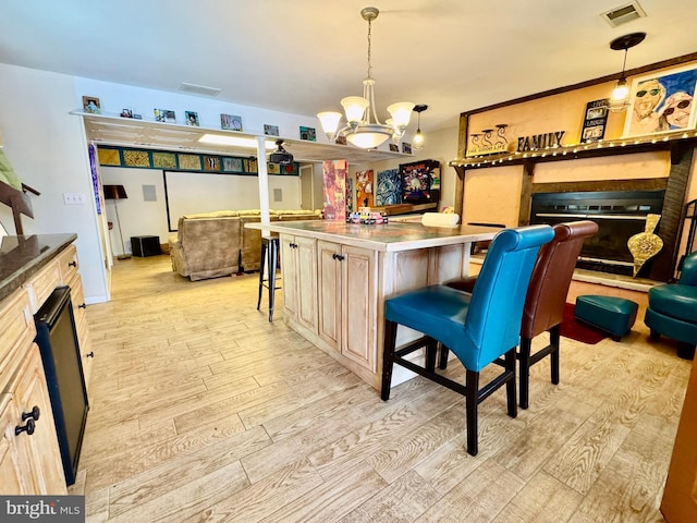 kitchen featuring light wood-style flooring, a kitchen island, hanging light fixtures, a kitchen bar, and a glass covered fireplace