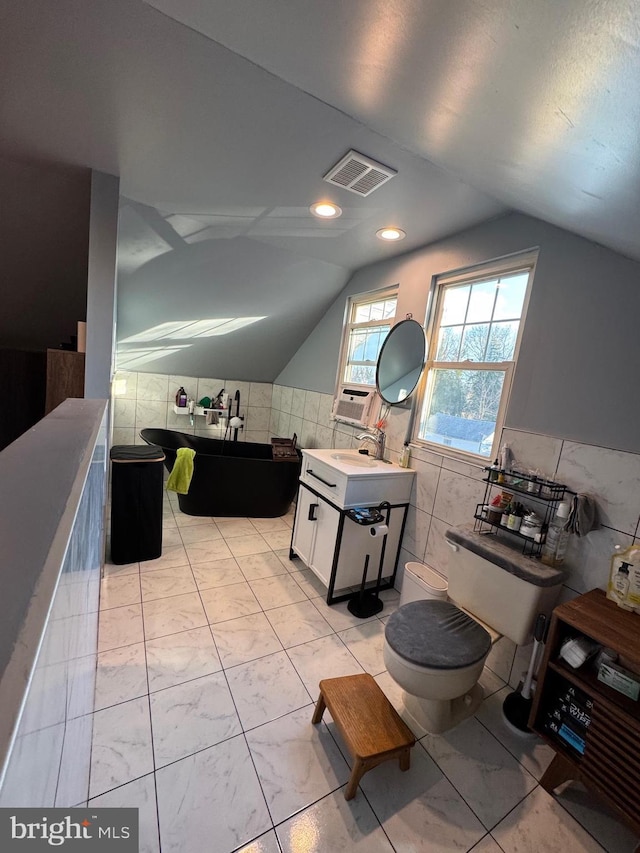 bathroom featuring tile walls, visible vents, toilet, vaulted ceiling, and a freestanding tub