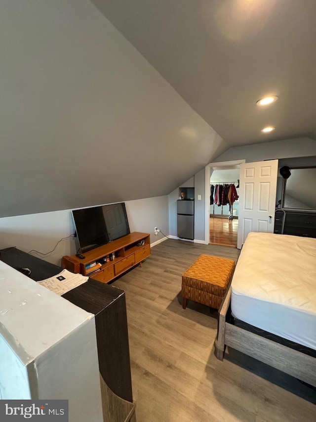 bedroom with baseboards, lofted ceiling, wood finished floors, freestanding refrigerator, and recessed lighting