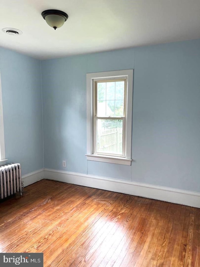 empty room with light wood finished floors, radiator heating unit, visible vents, and baseboards