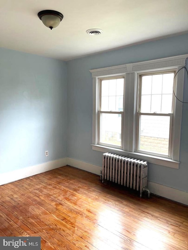 empty room with baseboards, radiator heating unit, visible vents, and light wood-style floors