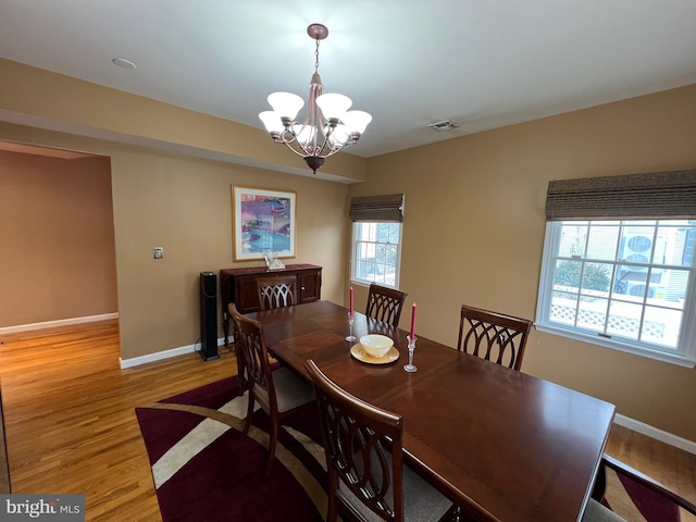 dining space featuring baseboards, a chandelier, visible vents, and light wood-style floors