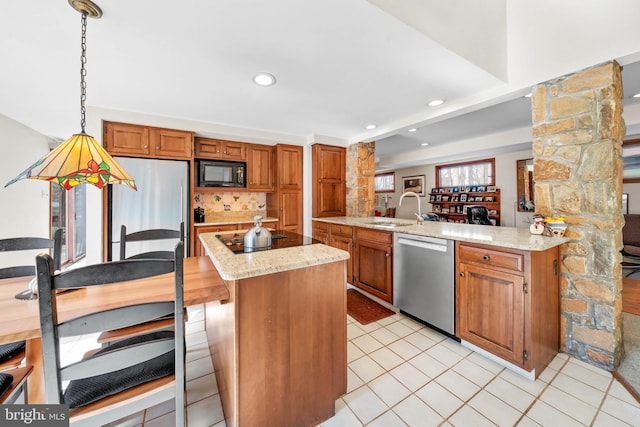 kitchen with light stone counters, hanging light fixtures, brown cabinetry, a sink, and black appliances