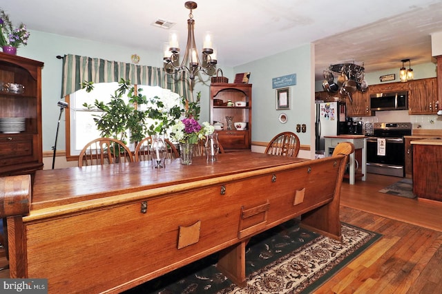 dining space with visible vents, an inviting chandelier, and wood finished floors