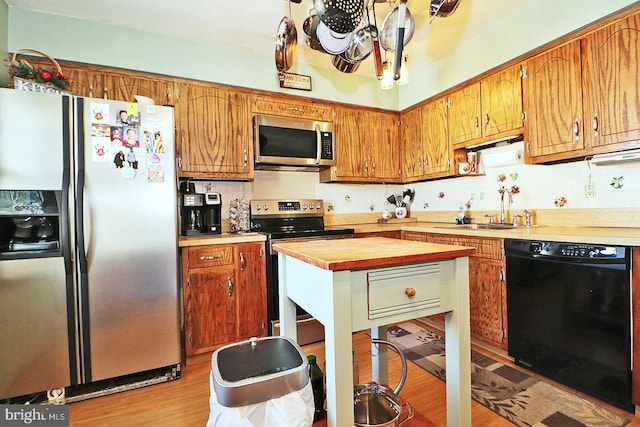 kitchen featuring light wood-style flooring, appliances with stainless steel finishes, brown cabinets, a sink, and backsplash