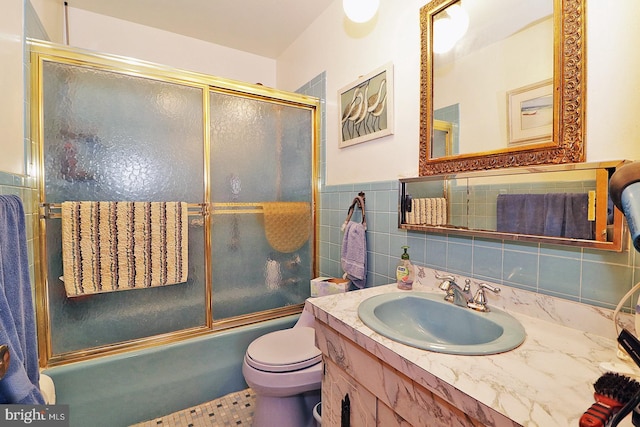 bathroom with toilet, vanity, tile walls, combined bath / shower with glass door, and wainscoting