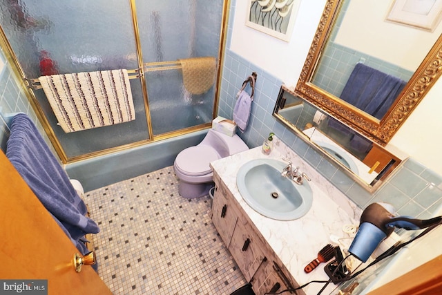 full bathroom featuring toilet, shower / bath combination with glass door, tile patterned floors, vanity, and tile walls