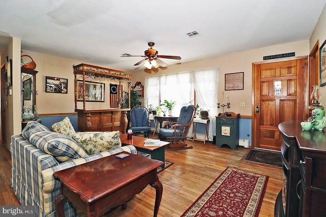 living area featuring a baseboard heating unit, ceiling fan, visible vents, and wood finished floors