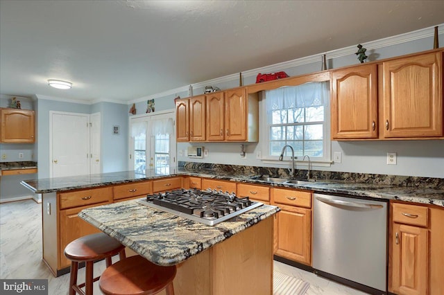 kitchen with appliances with stainless steel finishes, a sink, a peninsula, dark stone counters, and ornamental molding