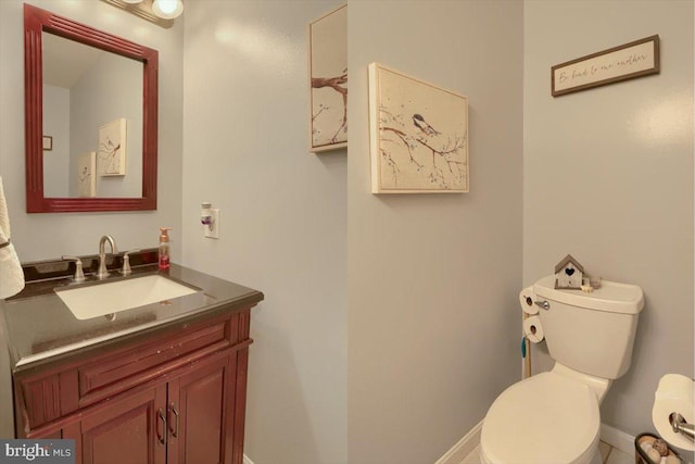 half bath with toilet, baseboards, and vanity