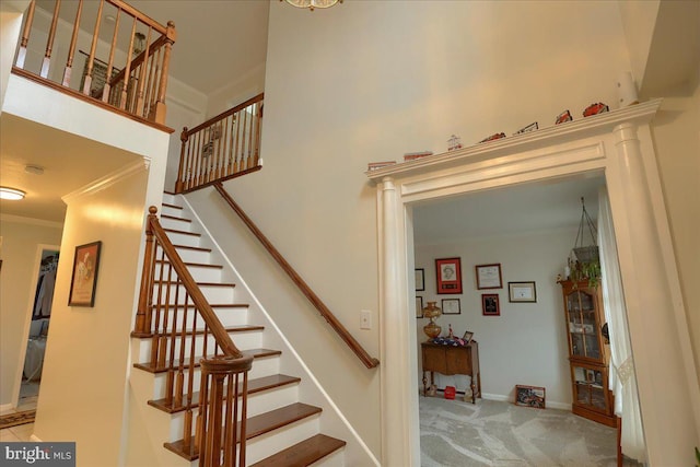 stairs featuring baseboards, a high ceiling, carpet, and crown molding