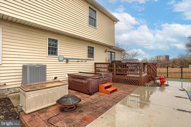 view of patio / terrace with central air condition unit, a wooden deck, a hot tub, and a fire pit