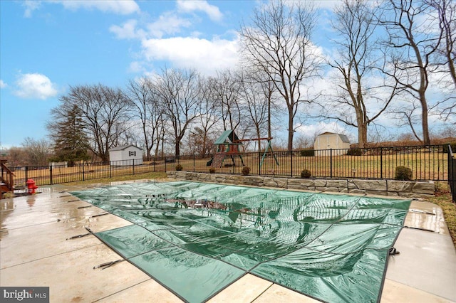view of pool with fence, playground community, a fenced in pool, a storage unit, and an outbuilding