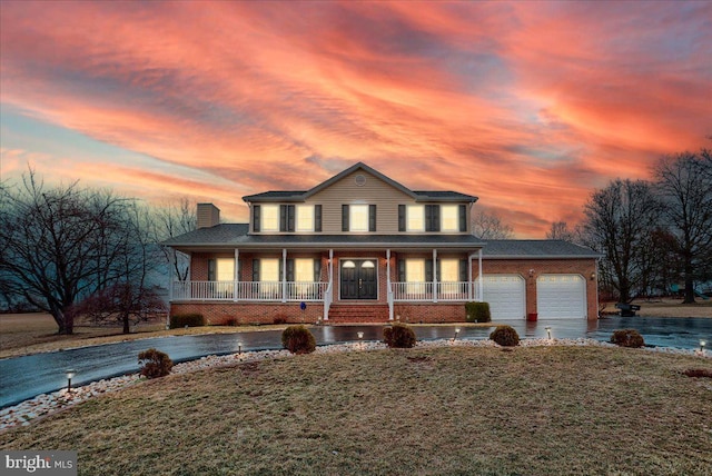 farmhouse-style home featuring covered porch, aphalt driveway, brick siding, a front lawn, and an attached garage