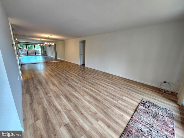unfurnished living room featuring wood finished floors, a chandelier, and baseboards