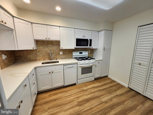 kitchen featuring white appliances, a sink, tasteful backsplash, light wood-style flooring, and white cabinets