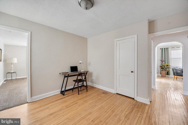 office area with light wood-style floors, arched walkways, a textured ceiling, and baseboards