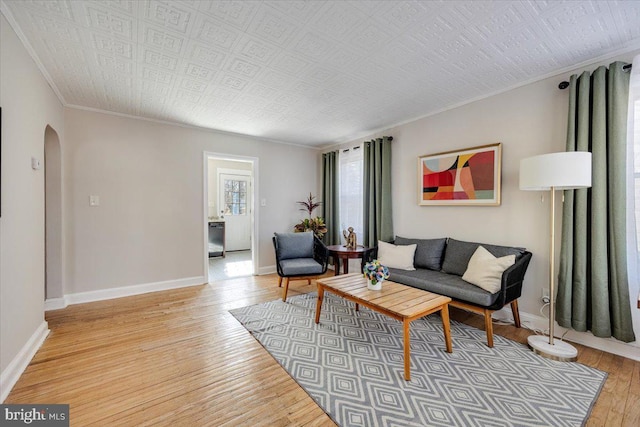 living area featuring light wood-type flooring, baseboards, arched walkways, and crown molding