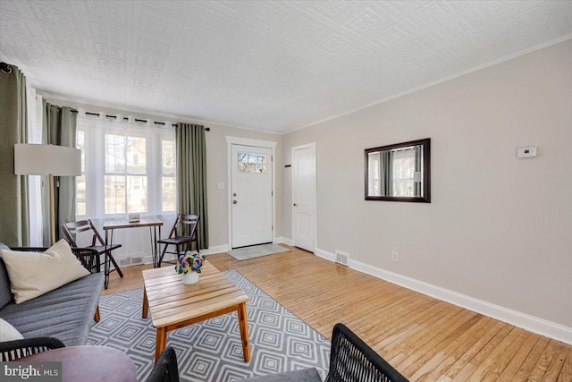 living area with light wood-style floors, baseboards, visible vents, and ornamental molding