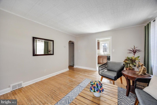 sitting room featuring arched walkways, visible vents, baseboards, ornamental molding, and light wood finished floors